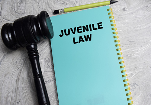 Gavel and handcuffs resting on a wooden block labeled JUVENILE LAW.